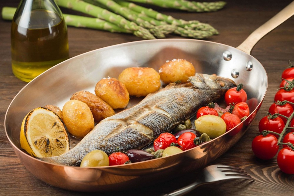 Запеченная рыба с овощами в посуде рядом со спаржей, вилка